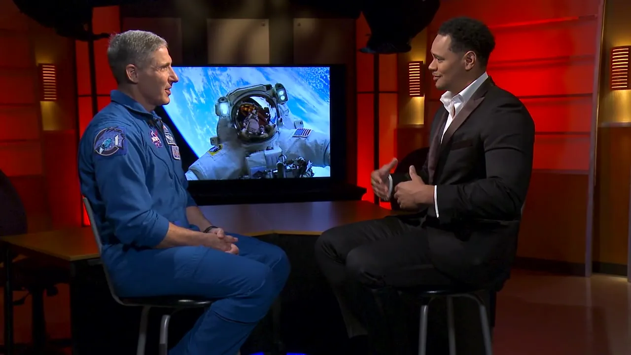 Kiva Geiger interviewing NASA astronaut Mike Hopkins in front of a screen showing a spacewalk